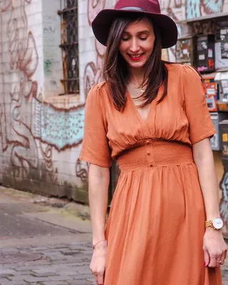 Orangefarbenes Sommerkleid mit Gürtel und Hut vor bemalter Wand